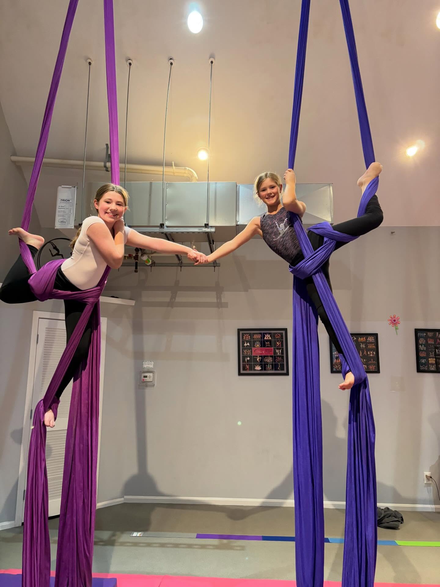 Two students holding hands while practicing on purple aerial silks