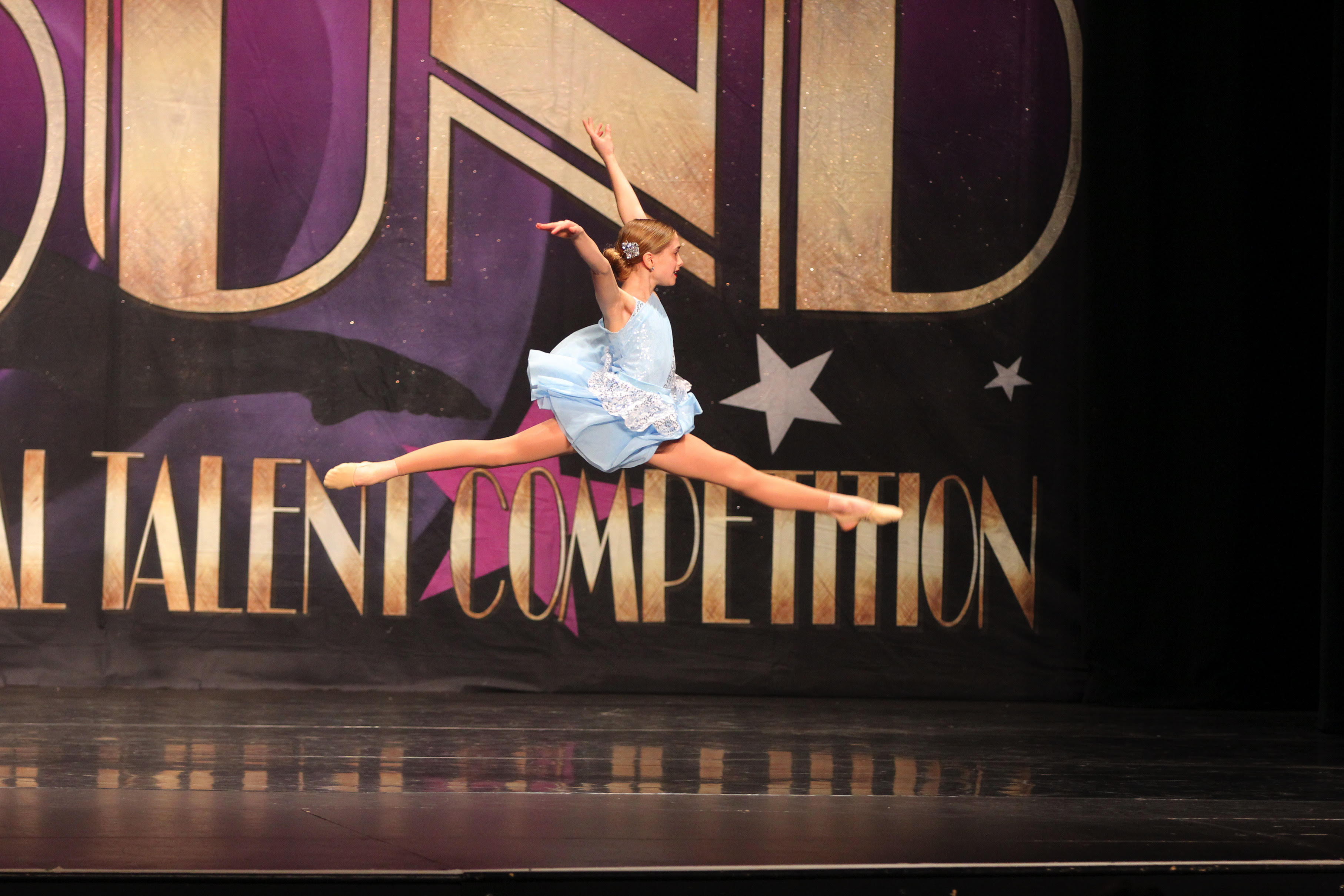 A dancer in a blue costume leaping across the stage