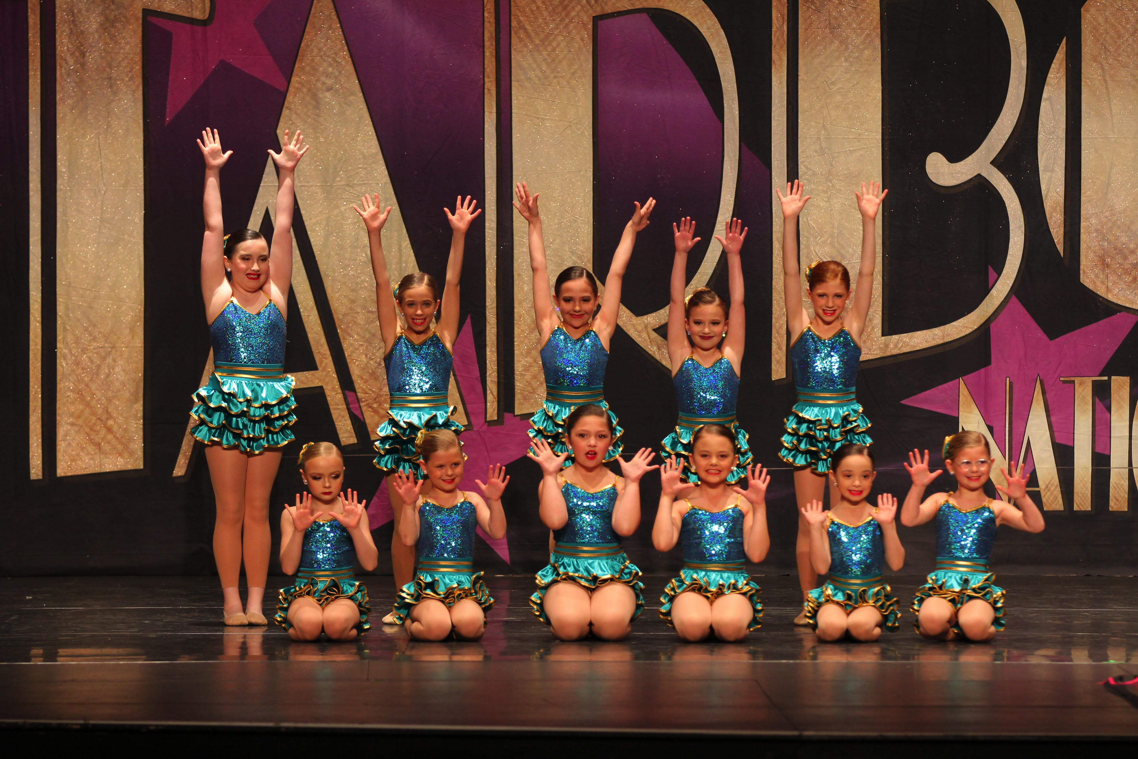 Young dancers in teal costumes celebrating together onstage