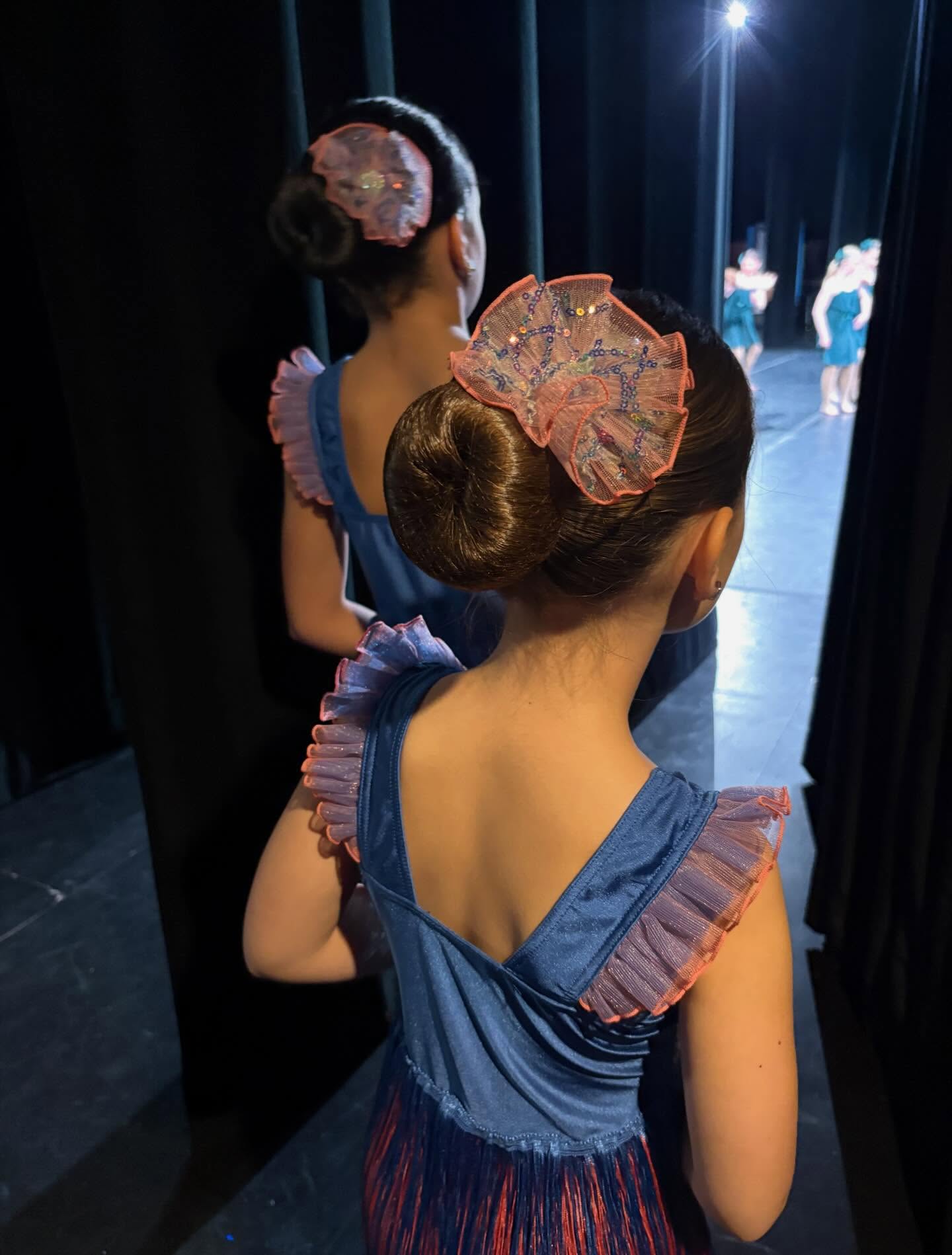 A young dancer in a blue costume waiting with a friend in the wings