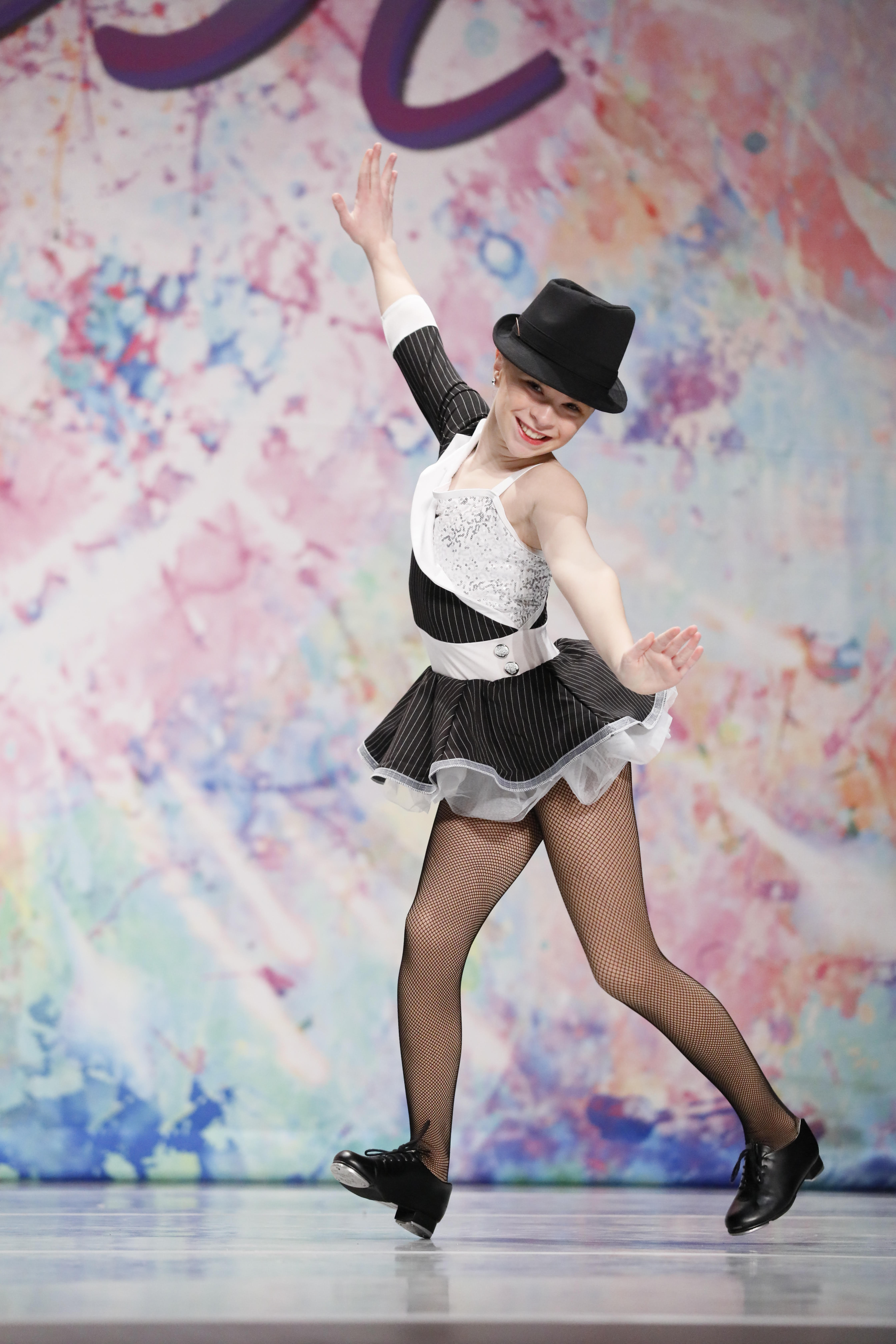 A smiling dancer performing in a black and white costume and hat