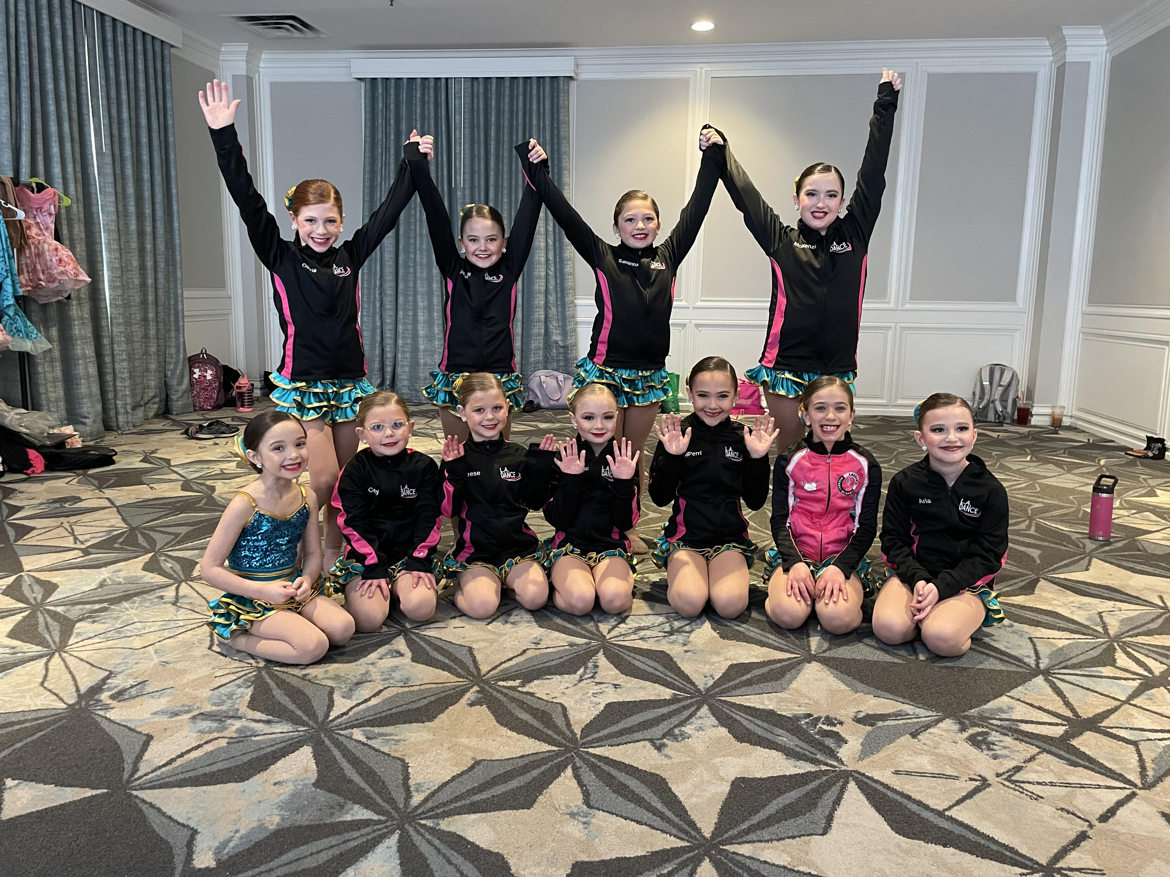 Young L.A. Dance teammates smiling together in their pink and black team jackets